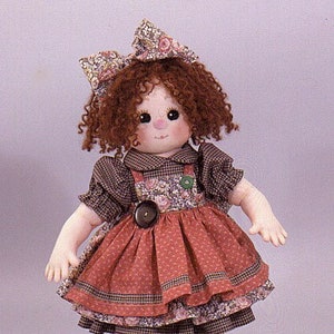 May include: A handmade rag doll with red curly hair, wearing a brown and white checked dress with a floral print apron, brown tights, and brown lace-up shoes.