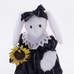May include: A white plush bunny wearing a blue plaid dress with a white lace collar and a blue bow. The bunny is holding a yellow sunflower and is wearing blue shoes with white fur trim.