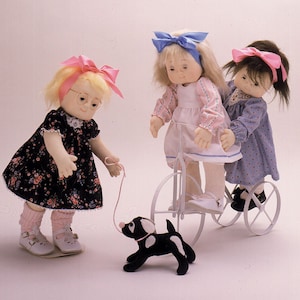 May include: Three dolls, one with pink and white glasses, are playing with a toy dog and a tricycle. The doll with glasses is wearing a black and white floral dress and pink socks. The doll on the tricycle is wearing a pink and white dress and has a blue bow in her hair. The doll behind her is wearing a blue and white dress and has a pink bow in her hair.