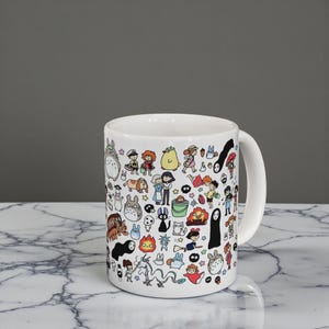 Detailed close-up of cute forest spirit characters and Kodama artwork printed on a ceramic coffee mug. Anime-inspired mug design influenced by Princess Mononoke and the magical nature themes of Studio Ghibli