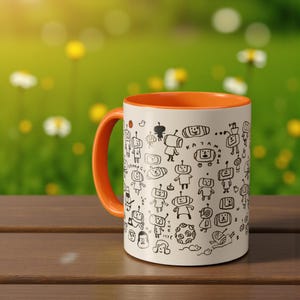 May include: White ceramic mug with an orange interior and handle. The mug features a repeating black and white doodle pattern of robot-like figures. The mug is sitting on a wooden surface with a blurred green background.