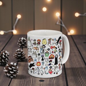 Aesthetic coffee mug with cute forest creatures and Kodama inspired design placed on a wooden table. Anime mug inspired by the whimsical fantasy style of Studio Ghibli and films like Spirited Away.