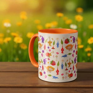 May include: A white ceramic mug with an orange handle and interior. The mug is decorated with colorful cartoon characters, flowers, and fruit. The mug is sitting on a wooden surface with a blurred green and yellow background.