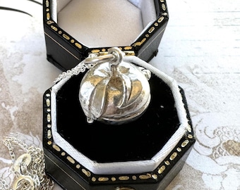 May include: A silver locket necklace with a leaf design. The locket is open and is sitting in a black velvet box with a gold trim.