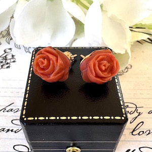 May include: A pair of rose-shaped coral earrings with gold settings. The earrings are displayed in a black velvet box.