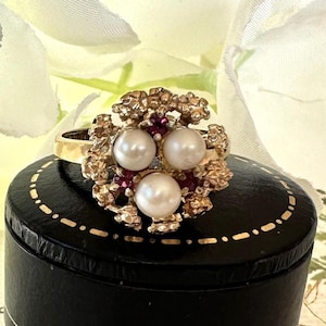 May include: A gold ring with a cluster of three white pearls and red gemstones set in a textured floral design.