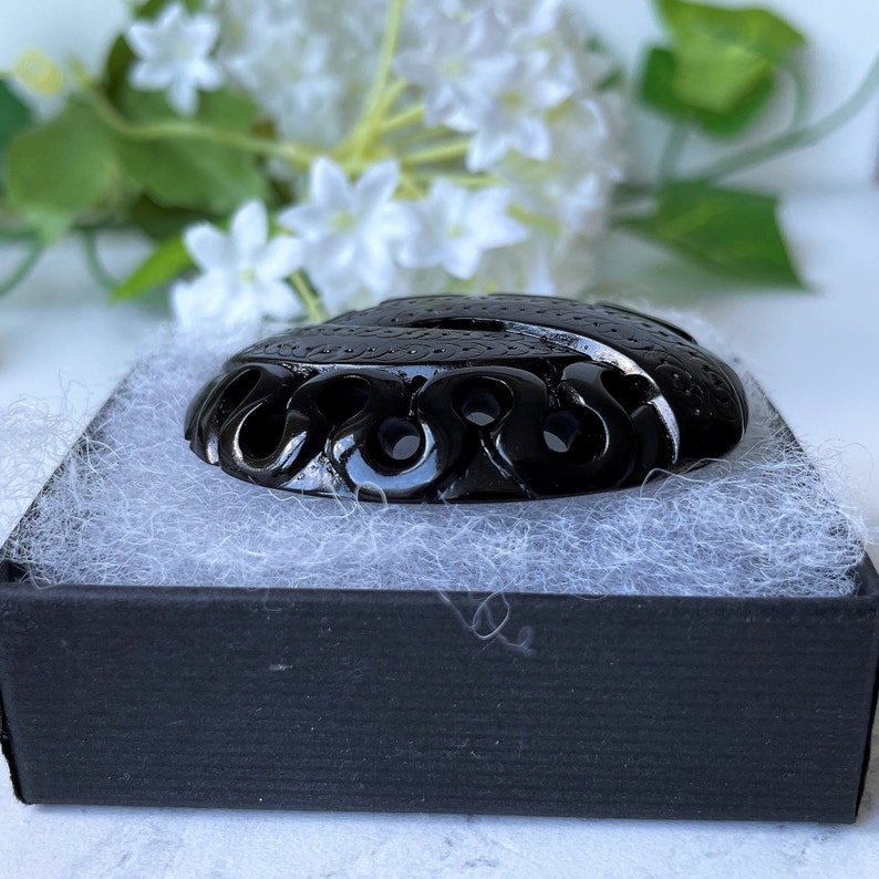 May include: A black carved pendant with intricate designs, displayed in a black box with white tissue paper.