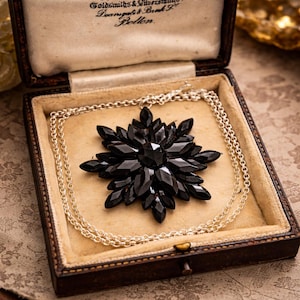 May include: A vintage black crystal pendant necklace in a brown jewellery box. The pendant is a starburst design with a large central stone and multiple pointed facets. The necklace chain is silver-toned.