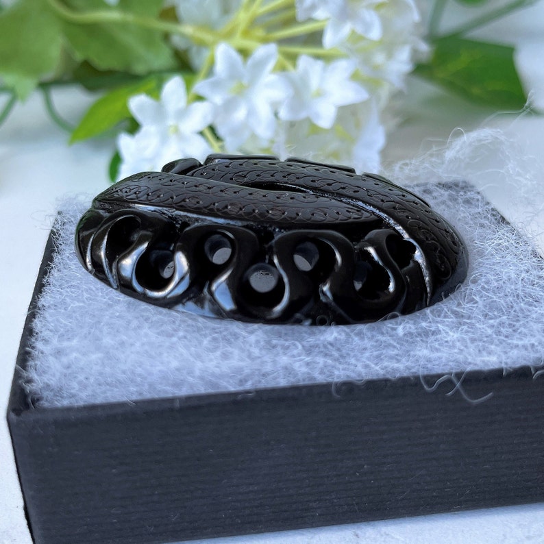 May include: A black carved pendant with intricate designs and openwork. The pendant is oval shaped and has a glossy finish.