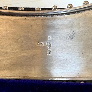 May include: Close-up of a silver hallmark on a silver object. The hallmark includes the letters "WAR" and a crown.