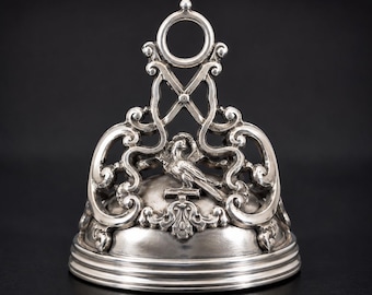 May include: A silver antique wax seal with intricate scrollwork and a bird motif. The seal features a ring handle and a detailed base, showcasing a classic design. The background is black.