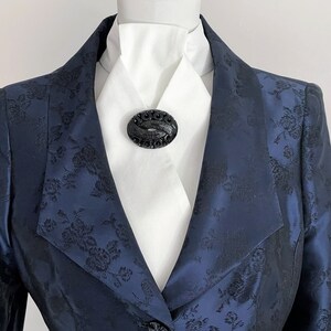 May include: A navy blue blazer with a black floral pattern and a black oval brooch on a white shirt.