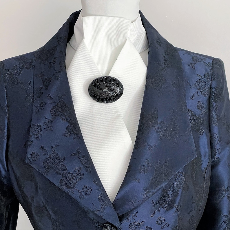 May include: A navy blue blazer with a black floral pattern and a black oval brooch on a white shirt.