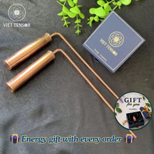 Op de afbeelding: Twee koperkleurige cilindrische staven met gedraaide handvatten, vergezeld van een donkerblauwe vierkante doos met het label VIET TENSOR Energy Frequency. Een ronde afbeelding toont een ring in een geschenkdoos met de tekst GIFT for you 333MHz.