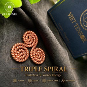 Pode incluir: Três ornamentos em espiral de cor cobre dispostos sobre uma superfície de tecido cinza. O texto "TRIPLE SPIRAL" é exibido abaixo das espirais, com texto adicional indicando "Triskelion of Vortex Energy". A marca "VIET TENSOR" é visível.