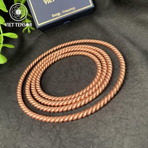 May include: Coiled copper-colored rope, possibly a necklace or decorative element. The rope has a twisted design and is arranged in concentric circles. The background is a dark, textured surface. The image also shows a box with the text "Energy - Frequency".