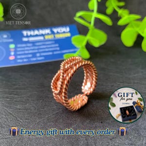May include: A copper-colored ring featuring a twisted rope design that forms an open knot pattern. The band has a textured, metallic finish with a continuous braided appearance throughout the entire circumference of the circular jewelry piece.