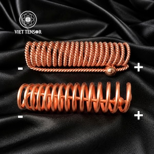 May include: Two copper-coloured metal hair accessories featuring a spiral coil design. The top piece has a tightly wound twisted wire texture with a small spherical end, while the bottom piece features a smooth, open-coil spring structure.