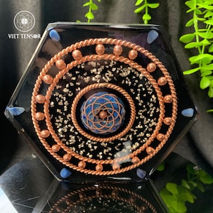 May include: Hexagonal black resin art piece with copper wire spirals and accents. The center features a blue stone with a geometric design. The piece is decorated with small silver flakes and blue stones around the edges. The text "VIET TENSOR" is visible.