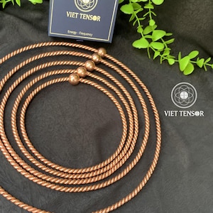 May include: Copper-colored tensor rings with small copper-colored spheres. The rings are arranged in a circular pattern on a dark surface. A navy blue box with the text "VIET TENSOR" is in the background.