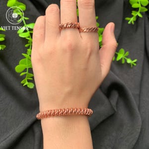 Op de afbeelding: Een koperkleurige armband en twee ringen met een spiraalontwerp worden op een hand getoond. De ringen zitten op de wijs- en middelvinger. De armband zit om de pols. De afbeelding bevat de tekst "VIET TENSOR".