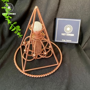 May include: A copper-colored geometric sculpture with a central sphere, intricate wire detailing, and a triangular frame. The sculpture is accompanied by a navy blue box with the text "VIET TENSOR" and the words "Energy - Frequency".