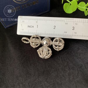 May include: A silver pendant with three ornate, circular designs connected by a central sphere. The pendant is approximately 1 inch in length. The design includes rope-like detailing and intricate patterns, suggesting a handcrafted or vintage style.