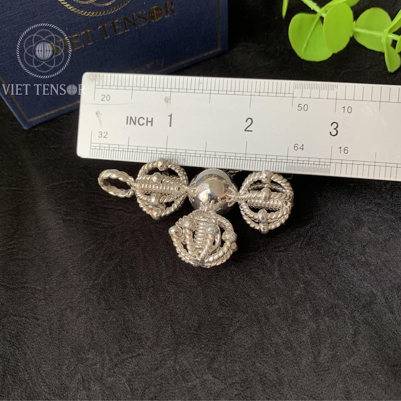 May include: A silver pendant with three ornate, circular designs connected by a central sphere. The pendant is approximately 1 inch in length. The design includes rope-like detailing and intricate patterns, suggesting a handcrafted or vintage style.