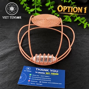 May include: A copper wire tensor device featuring a circular top and a central clear quartz crystal point wrapped in coiled copper wire. A blue business card is positioned in front with the text THANK YOU For choosing VIET TENSOR.