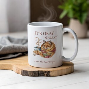 Cozy fox autumn mug in high-quality white ceramic, perfect for coffee, tea, or hot chocolate. Illustrated fox surrounded by autumn leaves, cottagecore and hygge style. A thoughtful gift for women or men, animal lovers, and woodland enthusiasts. Unique illustrated mug, durable, dishwasher and microwave safe, perfect for cozy fall vibes or as a seasonal gift idea for fox lovers and autumn home décor.