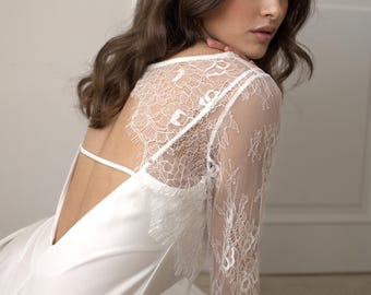 May include: A white satin gown with a low back and delicate spaghetti straps. The dress features intricate white lace detailing on the upper back and sleeves, creating an elegant and romantic look.