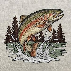 May include: Embroidered image of a rainbow trout leaping from water, with a backdrop of evergreen trees. The fish has detailed scales and orange and red markings. White water splashes surround the fish, and the background is a muted green.