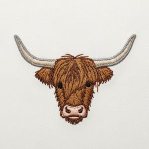 May include: Embroidered patch featuring the head of a Highland cow. The patch has a brown and tan color scheme, with long, shaggy fur and curved horns. The cow's face is detailed with black eyes and a pink nose.