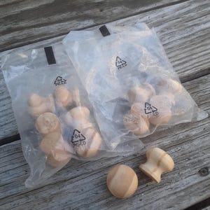 May include: Two clear plastic bags filled with small wooden knobs. The bags have a recycling symbol with the number 04 and the letters PE-LD printed on them. Two wooden knobs are outside of the bags.