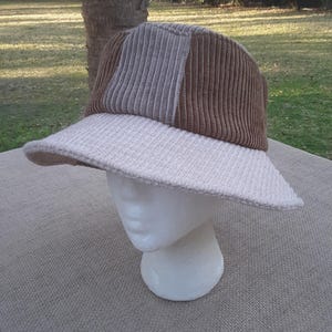 May include: A brown and beige corduroy bucket hat with a wide brim. The hat is made of a soft, textured fabric.