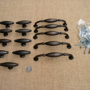 May include: A set of 12 cabinet pulls in a brushed bronze finish. The pulls are a combination of two styles: 3 inch long pulls and 1.5 inch long pulls. The set also includes screws for installation.
