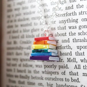 May include: A rainbow-coloured stack of miniature books on a silver chain necklace. The books are arranged in order of the rainbow colours, with the top book being red and the bottom book being purple.