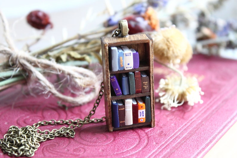 A small dark wooden bookshelf with three shelves of multicoloured books, strung on a bronze chain.