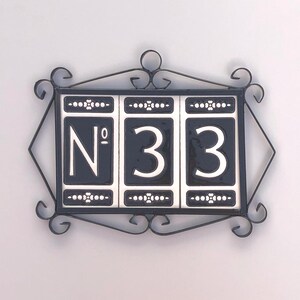 Peut inclure: Panneau de numéro de maison noir et blanc affichant "N° 33". Le panneau est encadré par une bordure décorative en fer forgé avec des volutes. Idéal pour une maison.