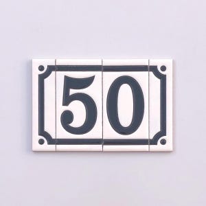 May include: White ceramic house number sign with the number 50 in dark gray. The sign is rectangular, composed of four tiles, and has a dark gray border with decorative corner accents.