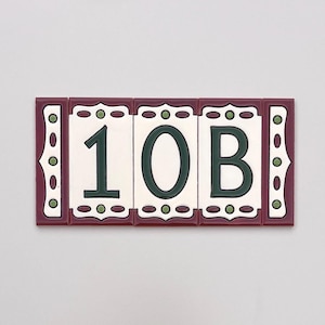 May include: Rectangular ceramic address tiles displaying the numbers "10B". The tiles have a white background with dark green numbers and a decorative border in burgundy and white with green accents. The tiles are arranged horizontally.