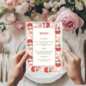 May include: A wedding menu card with a floral border featuring red and pink flowers. The menu card is held over a white plate with gold cutlery and surrounded by pink flowers. The menu includes starters, mains, and desserts.