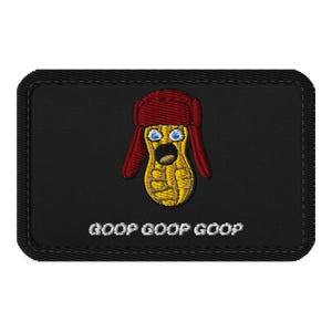 Puede incluir: Un parche rectangular negro bordado que presenta un personaje de cacahuete amarillo con un gorro de trampero rojo, ojos azules y la boca abierta. El texto GOOP GOOP GOOP está bordado en blanco debajo del personaje sobre el fondo negro.