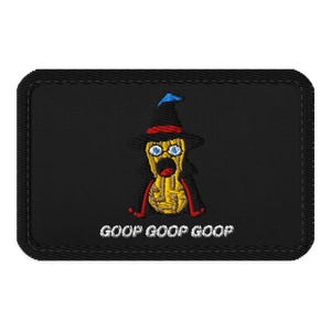 May include: A rectangular black embroidered patch featuring a yellow peanut character wearing a black witch hat with a blue tip and a red band, a black cape, and glasses. The text GOOP GOOP GOOP is embroidered in white below the character.