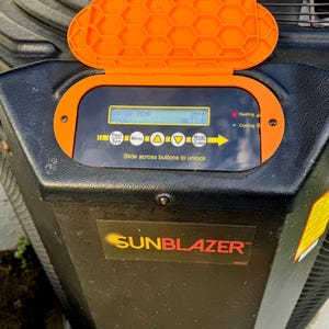 May include: A black SunBlazer pool heater with an orange control panel cover. The display shows the water temperature at 85°F and the word ACTIVE. The text "Slide across buttons to unlock" is visible.