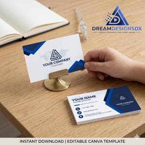May include: Business card design with a white background and blue geometric accents. The card features a company logo, contact information, and the text "YOUR COMPANY YOUR NAME". The business card is displayed on a wooden surface.
