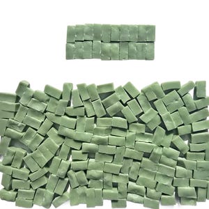 May include: A collection of small, rectangular, sage green mosaic tiles. The tiles are scattered across a white surface, with a smaller group arranged in a rectangular pattern above. These tiles are suitable for various craft and home decor projects.