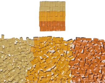 May include: A collection of small, rectangular, glossy tiles in shades of cream, yellow, and orange. The tiles are arranged in a neat, stacked rectangular block at the top, while a larger, scattered assortment of the same tiles fills the bottom.