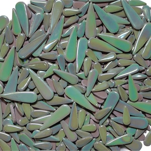 May include: A collection of iridescent, teardrop-shaped glass beads in shades of green, purple, and blue. The beads are scattered across a white background, creating a textured, organic pattern. These decorative beads are ideal for crafting and jewelry making.