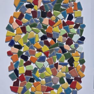 May include: A collection of colorful, irregularly shaped ceramic tiles in various colors, including red, blue, yellow, and green. The tiles are arranged in an oval shape against a white background, suggesting a mosaic or craft project.